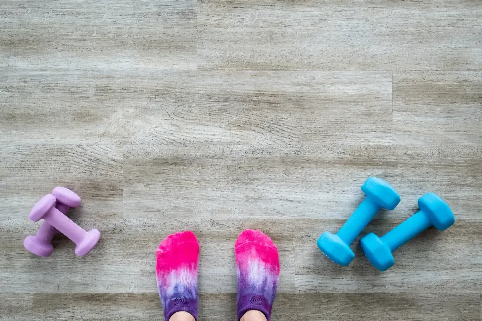 Kleine Hanteln auf dem Boden eines Trainingsraums, daneben zwei Füße in Sportsocken